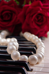 Keys of a piano with pearl necklace and bouquet of roses, selective focus.
