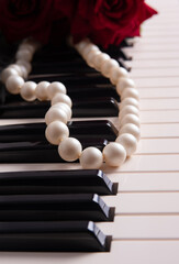 Keys of a piano with pearl necklace and bouquet of roses, selective focus.