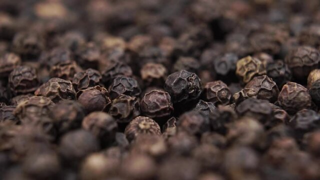 Peppercorns falling close up with rotation. Macro shot. Dried black pepper grains.