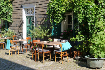 Two decorated tables with benches and chairs in front of a slate plated house with green shutters and decorated with plants