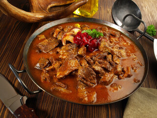 Wild Game Meat Goulash in a Pan with Cranberries on wooden Background