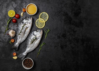Fresh fish dorado fish on black table with ingredients for cooking