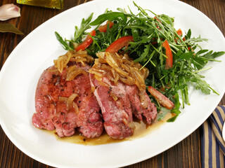 Roasted Veal Tongue Meat Slices with roasted Onions and Salad  on wooden Background