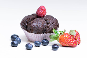 Baked chocolate muffin with juicy berries, strawberries, blueberries, raspberries.