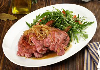 Boiled Veal Tongue Meat Slices with roasted Onions and Salad  on wooden Background