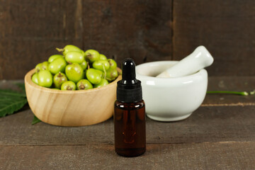 Neem oil in bottle with neem fruit in wooden bowl and mortar and pestle on wooden background.