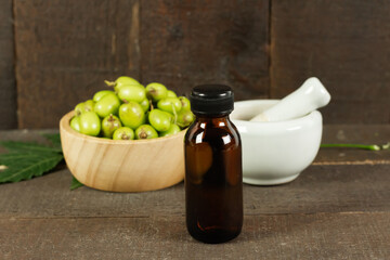 Neem oil in bottle with neem fruit in wooden bowl and mortar and pestle on wooden background.