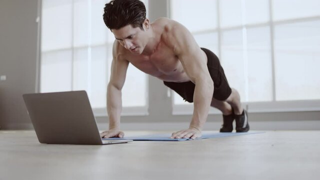 Man athletic trainer doing push up in gym And live teaching via laptop Or video call. Exercise strengthens the muscle. Workout take care of your health be in good shape. Distance teaching technology