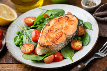 Grilled salmon steak served with healthy vegetable salad of baby spinach and cherry tomatoes. Healthy dinner meal