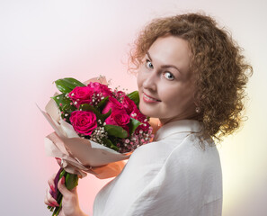 girl with curly hair in a white dress with a bouquet of flowers posing on a light background. concept of holidays and birthday.