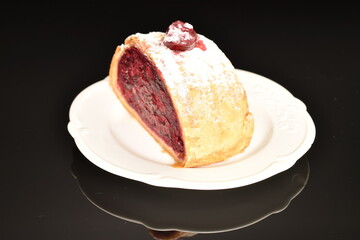 Fragrant cherry roll on a white ceramic saucer, on a black background.