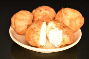 Tasty chouquettes with cream on a saucer, on a black background.