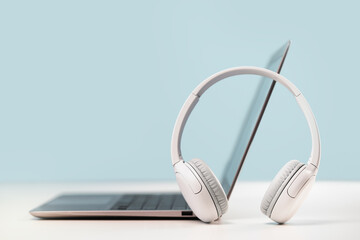 Side view of slim laptop with wireless headphones on grey desk. Blue background. Distant learning....