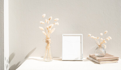 Blank mockup picture frame ,craft diary and dried flower in glass vase on beige table and cement wall background