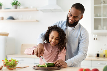 Cheerful african father teaching daughter how to cut veggies