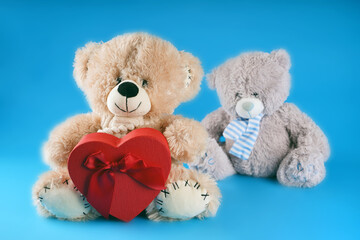 Close up of cute teddy bears with red gift box in form of heart. Soft plush toys with present on blue background. Concept of holidays, presents and good mood.