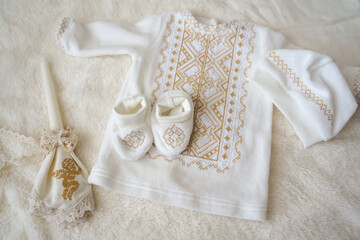 Accessories for the baptism of a child. Shirt, hat, shoes for the newborn, a candle decorated with an angel