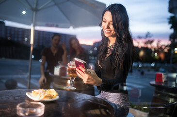 woman loking smartphone in bar terrace while drinking beer