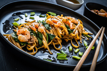 Asian food - noodles with prawns in soy sauce with spinach on black table
