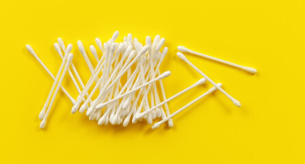 Pile of cotton buds or swabs on light yellow desk, view from above