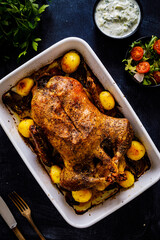 Roast duck in pot with vegetables on black wooden table
