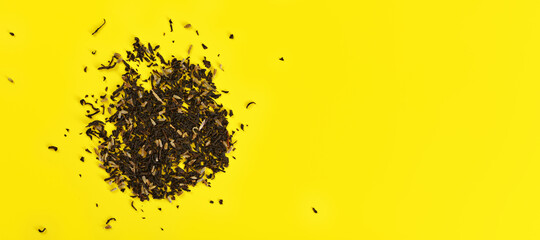 Loose black tea with few dried flowers on yellow board, view from above space for text right side