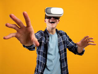 Excited young guy experiencing virtual reality in VR headset, making controlling gestures on orange background