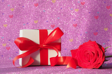 gift box with a red bow and a red rose on a purple glittering background. bokeh hearts..