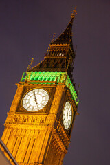 Fototapeta Big Ben clock face illuminated at night with dark skies behind with orange and green lights on the clock of Elizabeth Tower next to the Houses of Parliament in Westminster,, London, England obraz