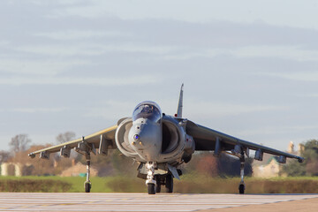 Harrier Jump Jet taxis towards the camera crossing the runway. Small vertical take and landing strike fighter - obrazy, fototapety, plakaty