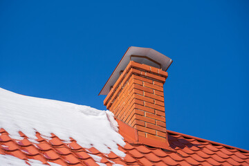Red roof of a detached house and chimney and snow against the blue sky in winter