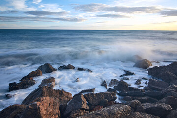 Fototapeta na wymiar A closeup shot of rocks in the wavy sea under a sunset sky