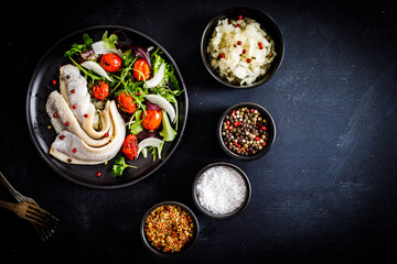 Marinated herrings with roast cherry tomatoes and fresh vegetable leaves on black table
