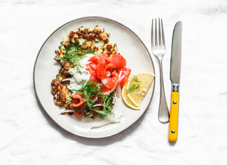Cauliflower fritters with smoked salmon and greek yogurt sauce on a light background, top view
