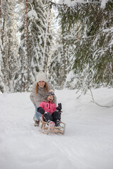 Fototapeta na wymiar Mother with daughter have fun in winter forest, riding on sledge and laughing.