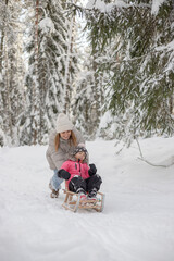 Fototapeta na wymiar Mother with daughter have fun in winter forest, riding on sledge and laughing.