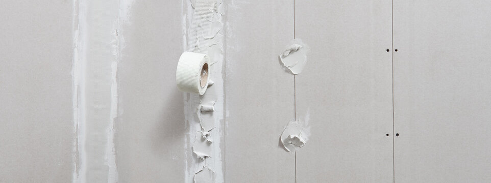 drywall construction repair concept, procedure for leveling plasterboard walls with stucco and mesh tape, wall with screws and plaster, useful for background layout with copy space