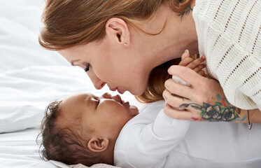 Young caucasian mother with tattoos kissing cute adorable african american small infant daughter...