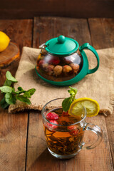 green tea in a glass cup with strawberries mint and lemon on a wooden table next to a teapot.