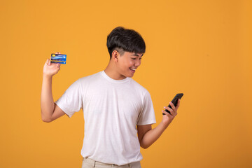 Image of a young man On orange background Happy Shopping on Light by paying by credit card Via mobile phone.
