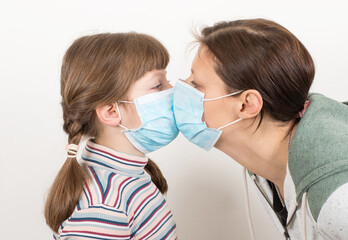 mother and daughter wearing a virus face mask kissing concept for corona virus