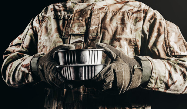 Photo Of Soldier In Camouflaged Uniform And Tactical Gloves Holding Canned Food Field Ration On Black Background.