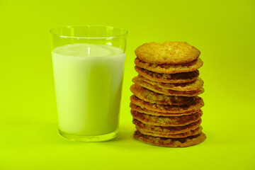 Glass of milk with cookies next to it making a tower, on a yellow background.