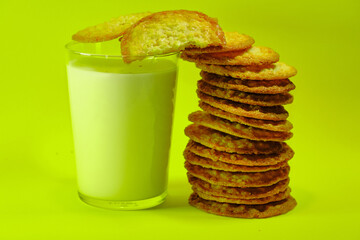 Glass of milk with cookies next to it making a tower, on a yellow background.