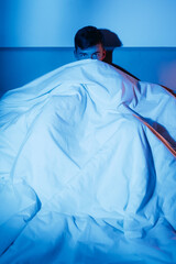Nightmare fear. Insomnia problem. Sleep disorder. Stress overwork. Man looking from blanket covering nose at night dark bedroom interior.