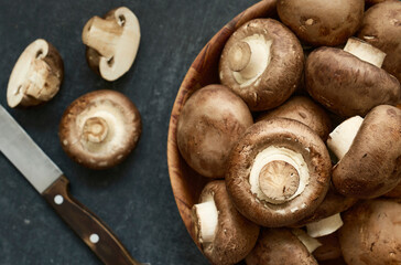 Fresh champignon mushrooms in a wooden bowl, closeup, top view, shallow depth of sharpness