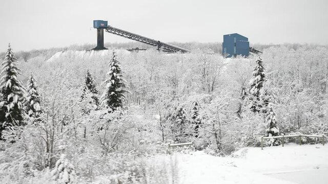 Slow motion passing snow covered landscape with coal mine elevators surrounded by forest in the winter.