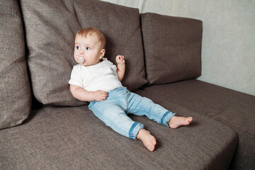 baby sprawled on couch with a baby's dummy in his mouth
