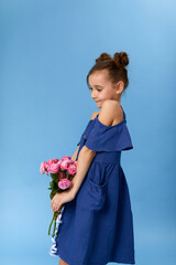 shy happy little girl holding bouquet of pink roses on blue background.