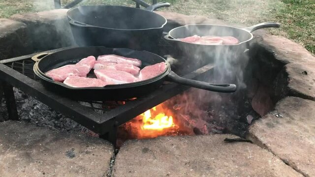 Cooking pork chops in Dutch oven cast iron skillets over an open campfire